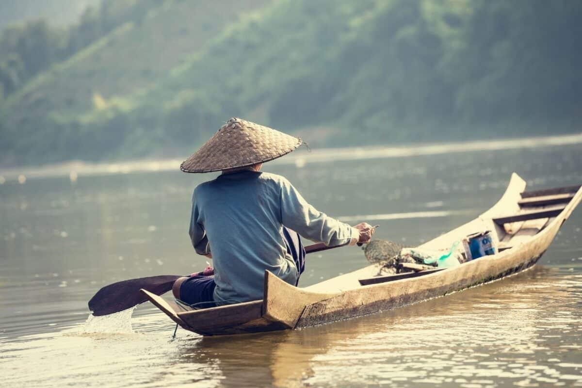 Homme pagayant sur une pirogue traditionnelle sur un fleuve au Laos.