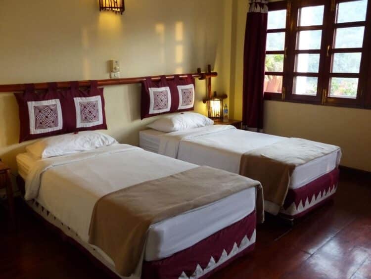 Chambre du Sanctuary Pakbeng Lodge avec lits jumeaux, textiles traditionnels et mobilier en bois.