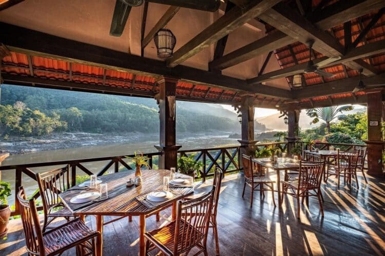 Restaurant en terrasse du Sanctuary Pakbeng Lodge avec tables en bois et vue sur le fleuve.