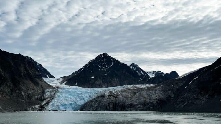 Glacier descendant entre montagnes sombres dans un fjord du Spitzberg sous un ciel couvert.