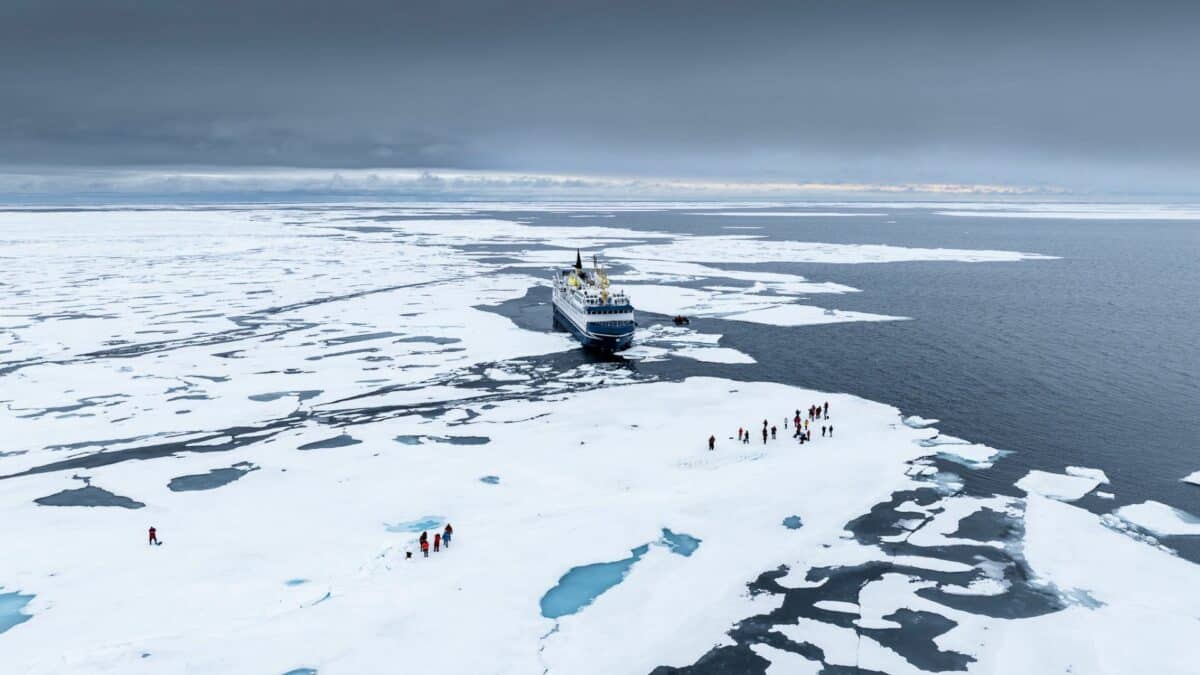 Navire d’expédition entouré de plaques de glace avec passagers débarqués sur la banquise au Spitzberg.
