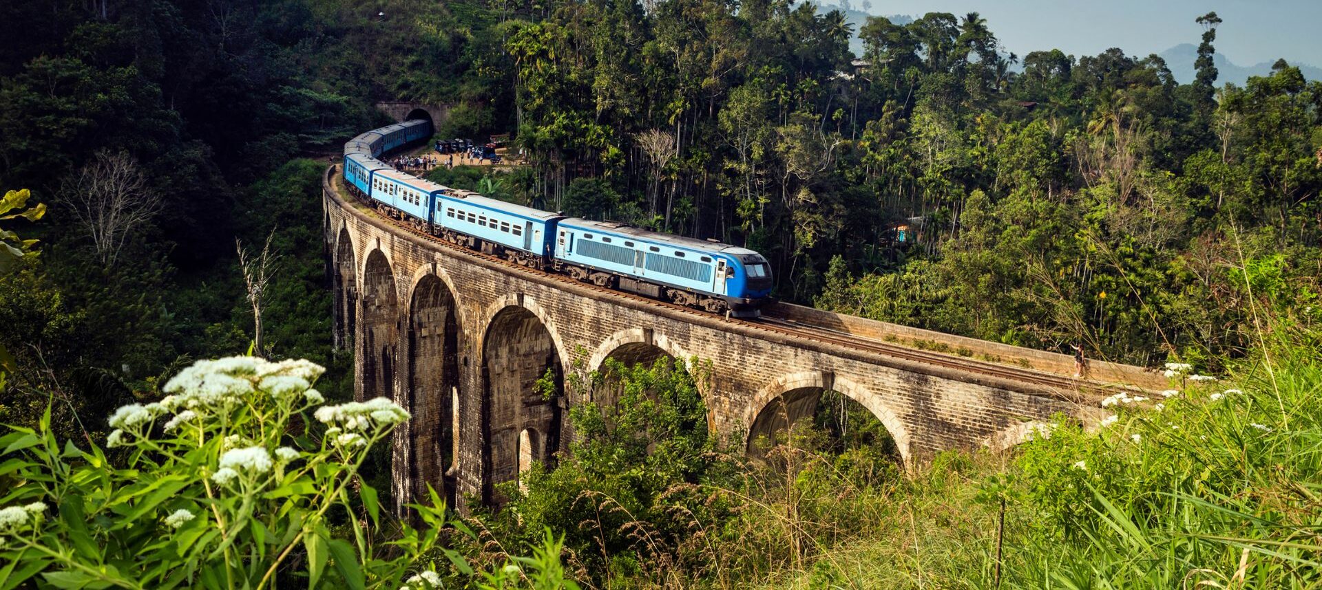 Train bleu traversant un viaduc en pierre au milieu de la jungle et des collines verdoyantes au Sri Lanka