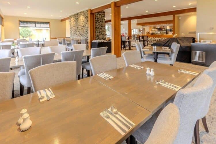 Salle de restaurant du Kingsgate Hotel Te Anau avec tables dressées et espace bar en arrière-plan.