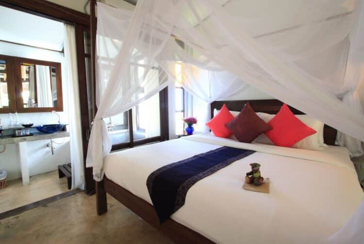 Chambre traditionnelle thaïlandaise avec lit à baldaquin et moustiquaire.