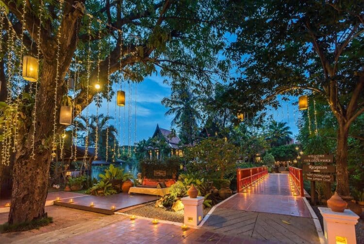 Allée illuminée et pont décoratif au sein de l’hôtel Legendha à la tombée de la nuit.