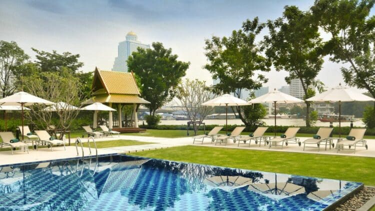 Piscine extérieure au bord du fleuve à Bangkok avec transats et parasols.