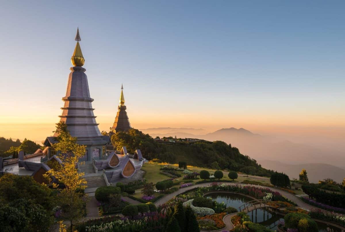 Stupas bouddhistes au sommet d’une montagne en Thaïlande, entourés de jardins et de brume.
