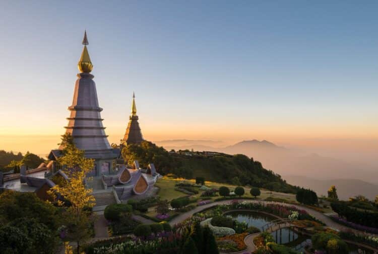 Stupas bouddhistes au sommet d’une montagne en Thaïlande, entourés de jardins et de brume.