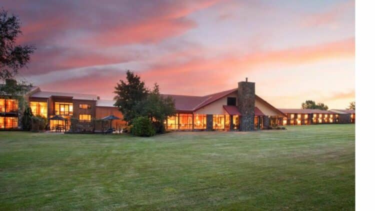 Extérieur du Distinction Mackenzie Country Hotel à Twizel avec bâtiment et pelouse au coucher du soleil.