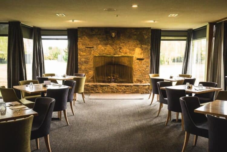 Salle de restaurant du Distinction Mackenzie Country Hotel avec cheminée en pierre et tables dressées.