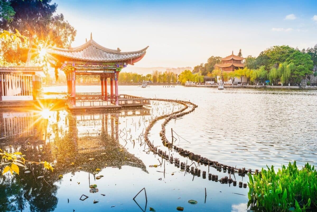 Pavillon traditionnel au bord d’un lac entouré de végétation dans le Yunnan