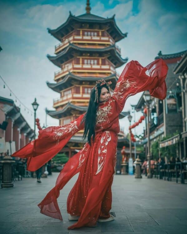 Femme en robe traditionnelle rouge dansant devant une pagode chinoise