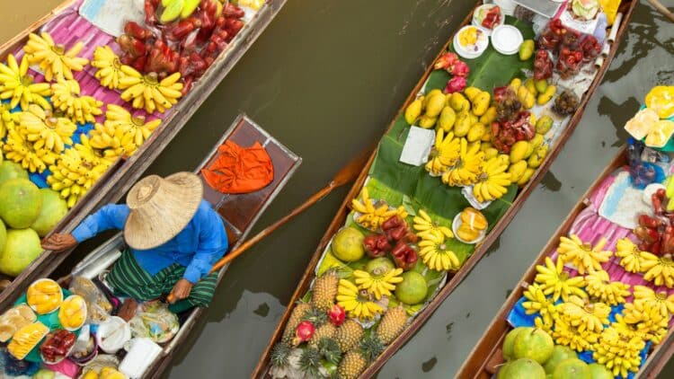 Bateaux remplis de fruits tropicaux sur un marché flottant en Thaïlande avec vendeur portant un chapeau traditionnel