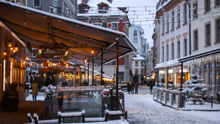 Rue du centre historique de Riga décorée de lumières hivernales avec neige et terrasses illuminées