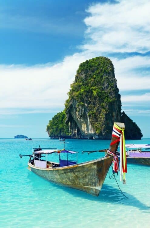 Bateau longtail sur une plage en Thaïlande avec eau turquoise et îlot rocheux