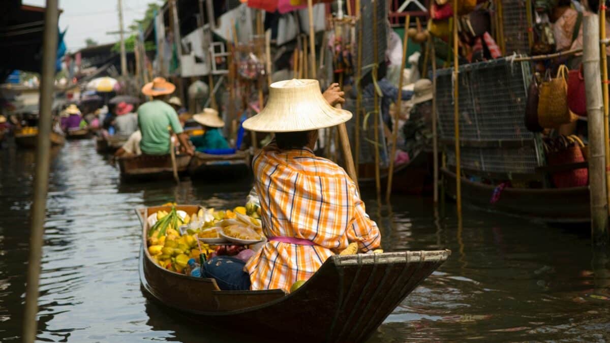 Vendeuse sur un bateau chargé de fruits dans un marché flottant en Thaïlande