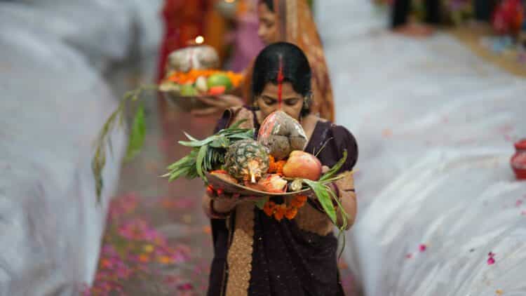 Femme réalisant un rituel religieux avec offrandes de fruits, fleurs et bougie dans un contexte traditionnel en Inde