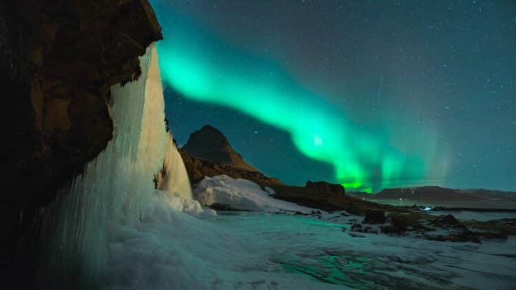 aurores boreales vertes au dessus dune cascade gelee en islande la nuit