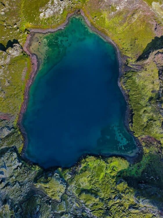 vue aerienne dun lac volcanique en islande entoure de reliefs verdoyants