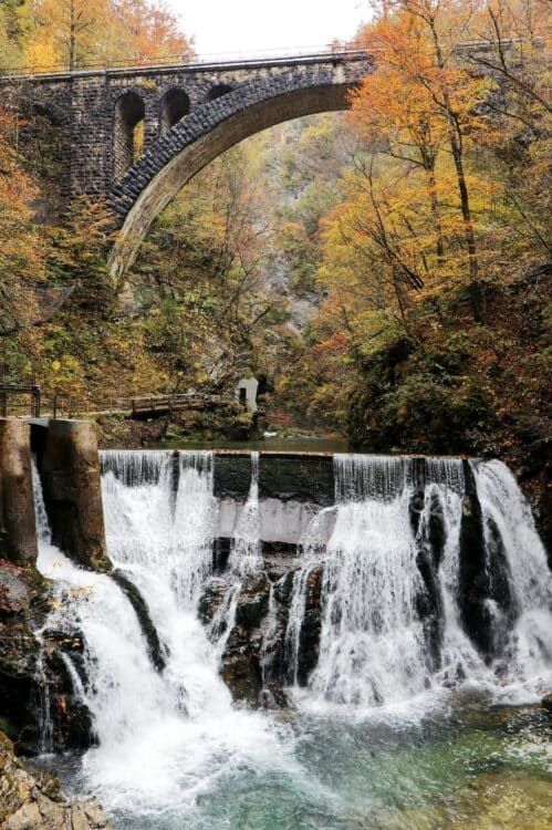 Pont en pierre au-dessus d’une rivière avec cascade dans une forêt aux couleurs d’automne en Slovénie