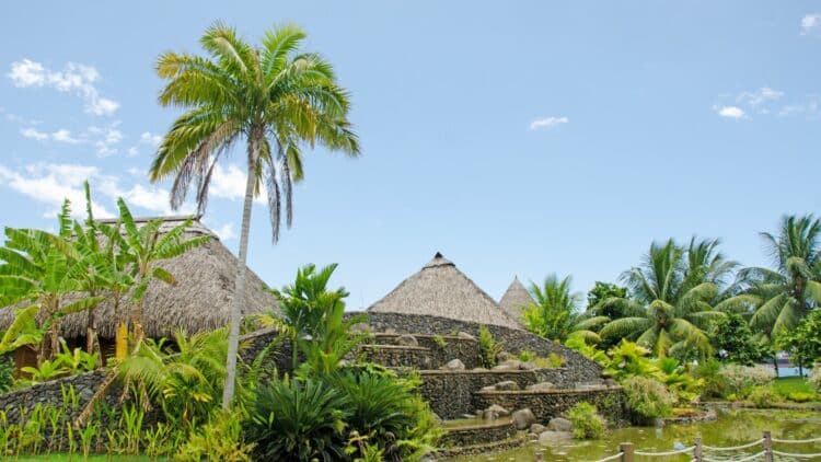 jardin tropical avec végétation luxuriante et habitations traditionnelles en Polynésie