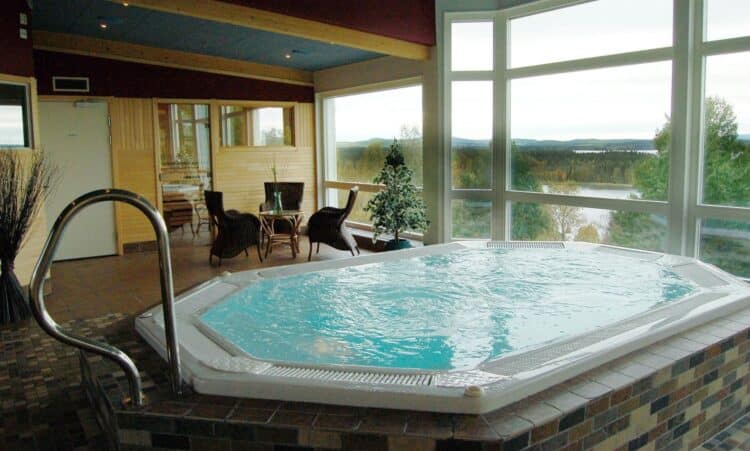 Jacuzzi intérieur d’hôtel avec grandes baies vitrées donnant sur un paysage naturel en Suède