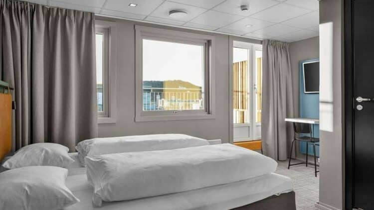 Chambre d’hôtel moderne en Norvège avec lit double et vue sur un fjord depuis un balcon