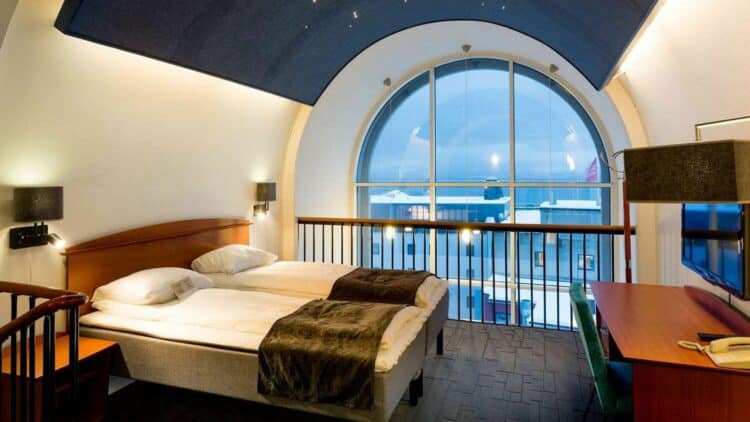 Chambre d’hôtel en Norvège avec plafond voûté et grande fenêtre panoramique sur extérieur
