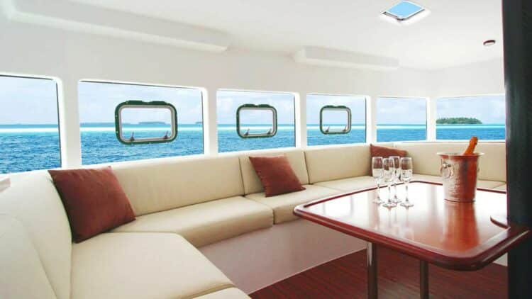 Salon intérieur d’un catamaran de luxe avec banquettes et vue sur la mer à travers les hublots