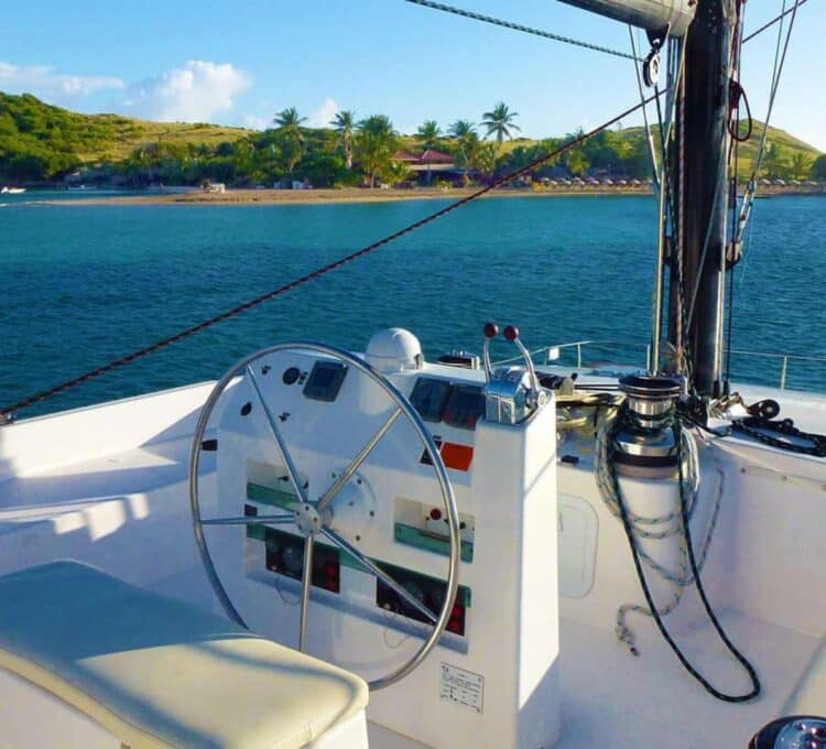Poste de pilotage d’un catamaran avec barre et instruments face à un lagon tropical