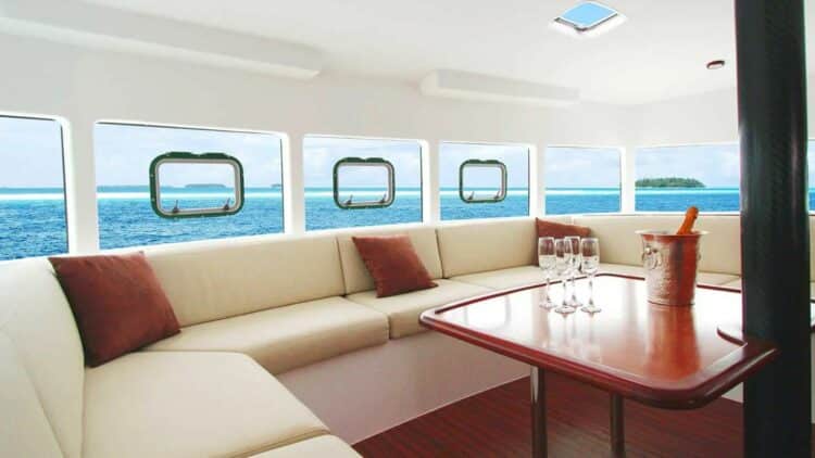 Salon intérieur de catamaran avec banquette et vue mer à travers les hublots