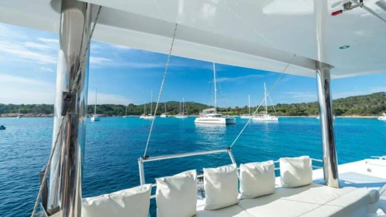 Espace extérieur d’un catamaran avec coussins et vue sur des bateaux au mouillage