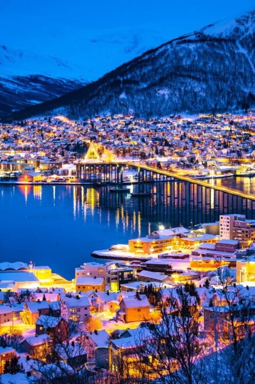 Vue de Tromsø en hiver de nuit avec pont illuminé et maisons enneigées