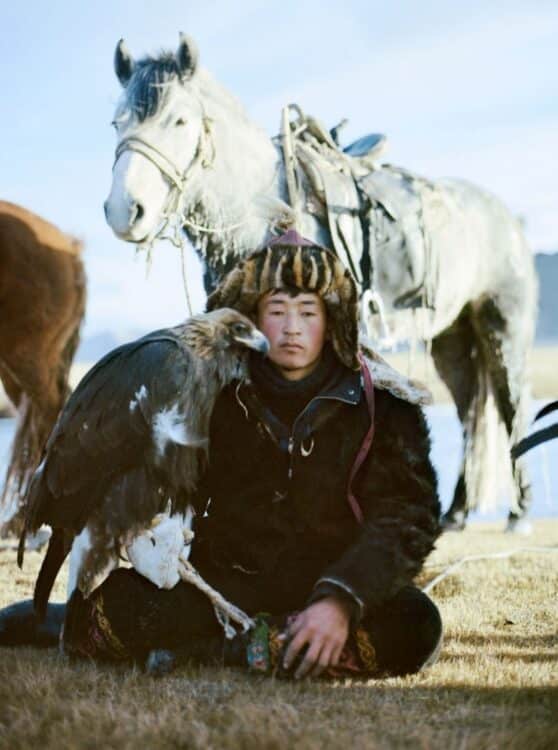 Chasseur à l’aigle mongol assis devant son cheval dans les steppes de Mongolie.