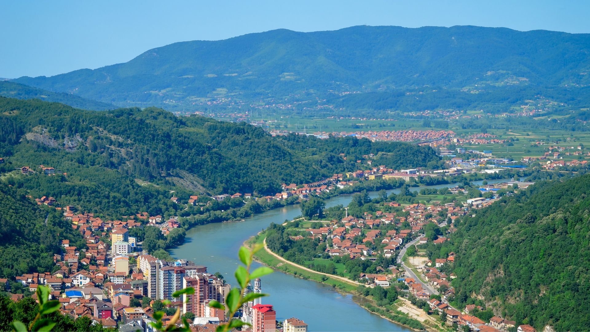 Vue panoramique sur une vallée traversée par une rivière en Bosnie-Herzégovine entourée de collines verdoyantes.