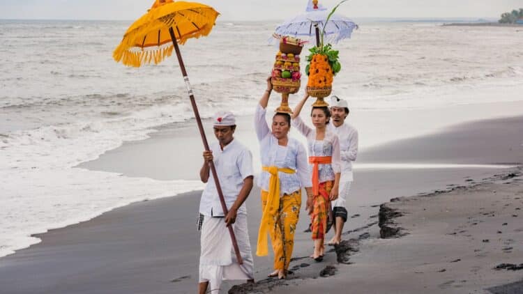 Cérémonie balinaise sur une plage avec des offrandes et des parasols traditionnels.
