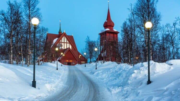 Église en bois rouge de Kiruna entourée de neige au crépuscule, en Laponie suédoise.