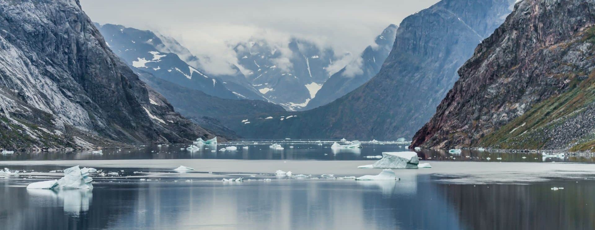 Fjord du Groenland parsemé d'icebergs entouré de montagnes rocheuses.
