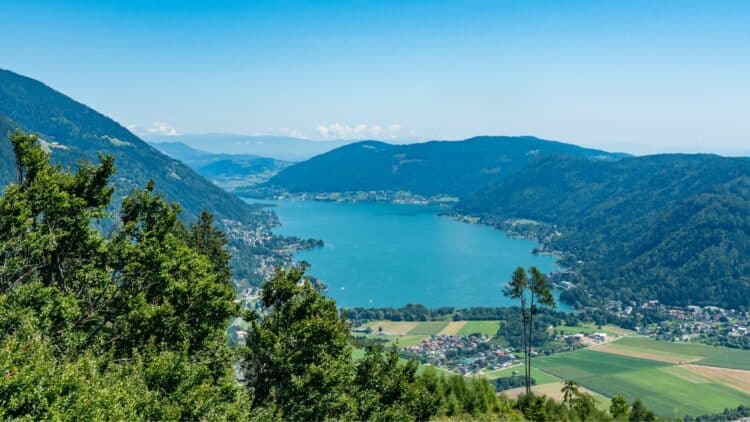 Vue panoramique sur un lac de Carinthie entouré de montagnes et de forêts.