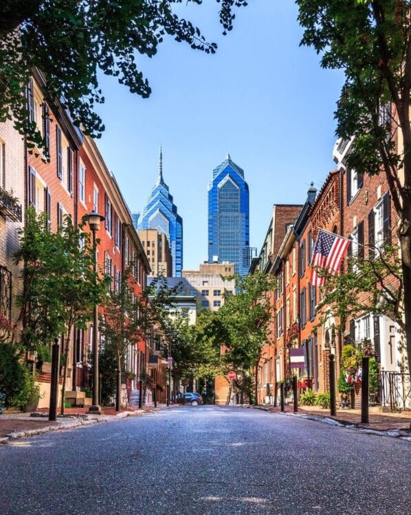 Rue bordée de maisons historiques avec le skyline moderne de Philadelphie en arrière-plan.