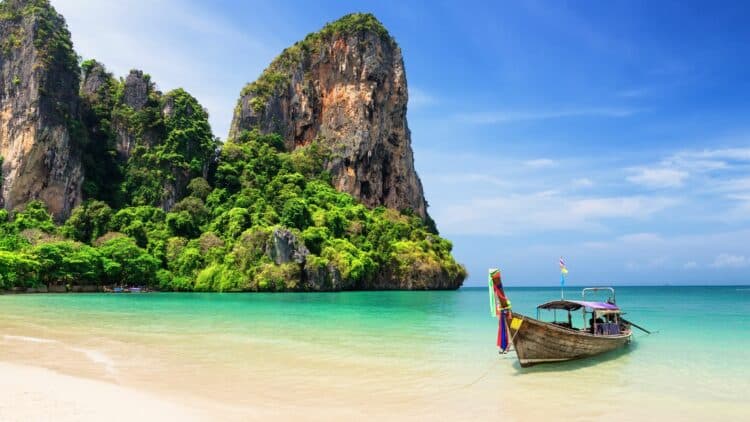Bateau traditionnel longtail sur une plage aux eaux turquoise en Thaïlande.