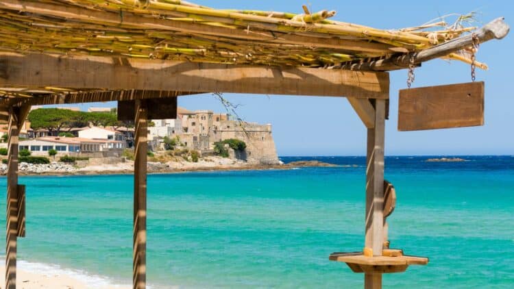Vue sur une plage aux eaux turquoise et une citadelle en Corse.