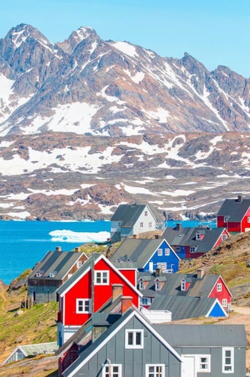 Maisons colorées d'un village côtier du Groenland face à un fjord et aux montagnes.