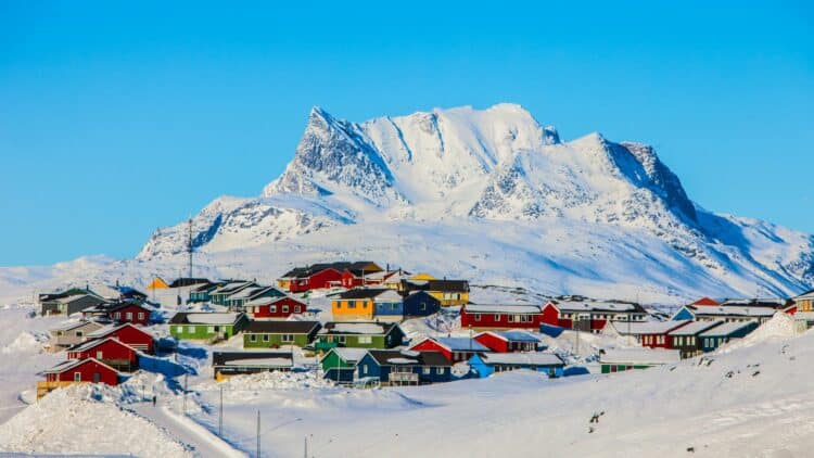 Village du Groenland sous la neige avec montagnes enneigées.