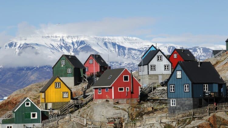 Maisons colorées d'un village du Groenland avec montagnes enneigées en arrière-plan.