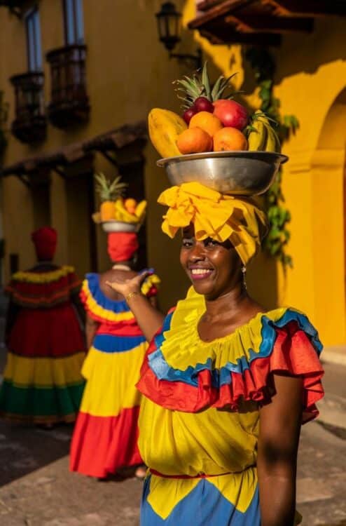Femme en tenue traditionnelle portant une corbeille de fruits à Carthagène.