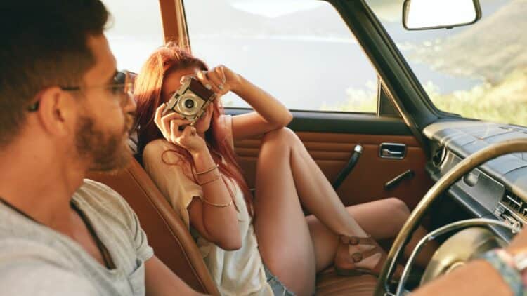 Couple en voiture lors d'un road trip, une femme prenant une photo.