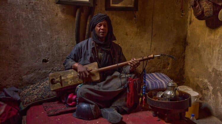 Musicien traditionnel marocain jouant d'un instrument dans un intérieur authentique.