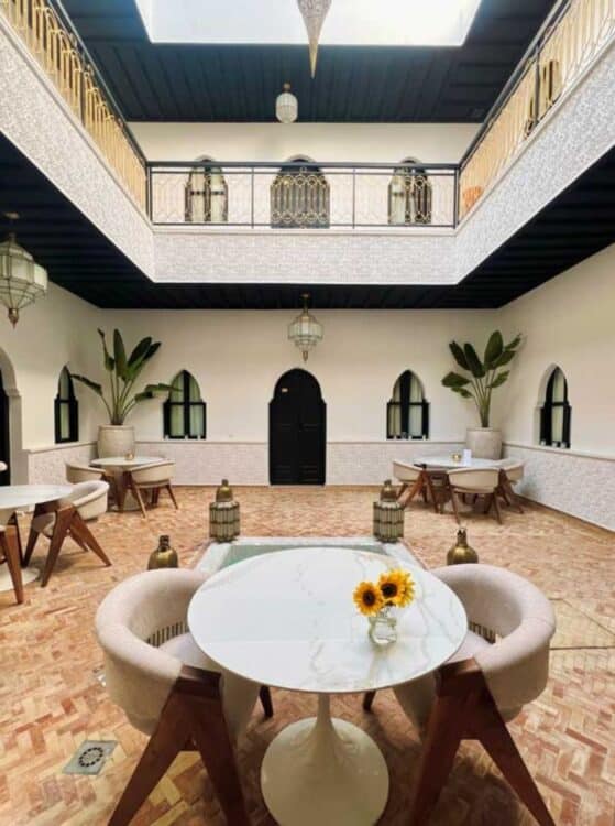 Patio lumineux d'un riad marocain avec tables et décoration traditionnelle.