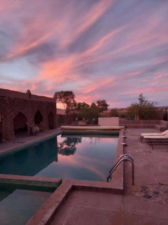 Piscine d'un riad marocain sous un ciel coloré au coucher du soleil.